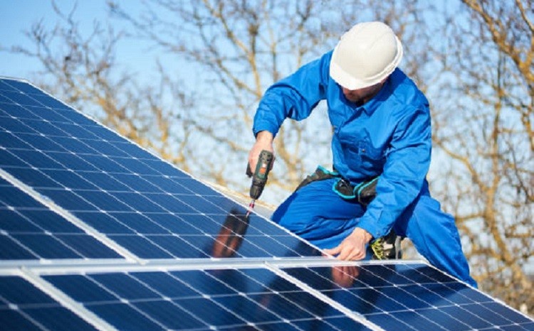 PV-solar-panel2 Male engineer in blue suit and protective helmet installing photovoltaic panel system using screwdriver. Professional electrician mounting solar module on roof. Alternative energy ecological concept.